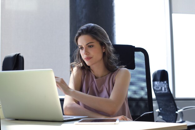 Mujer de negocios hermosa en ropa casual elegante trabajando en equipo portátil en la oficina.