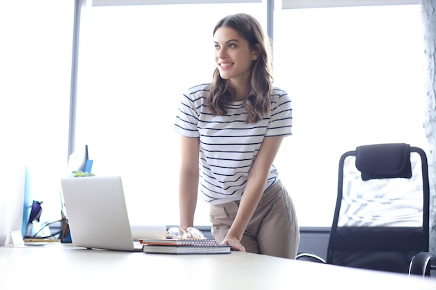 Mujer de negocios hermosa en ropa casual elegante trabajando en equipo portátil en la oficina.