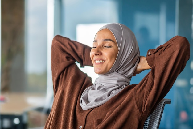 Mujer de negocios en hijab descansando mujer árabe en hijab con las manos detrás de la cabeza y sonriendo con