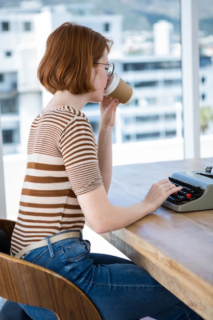 mujer de negocios hipster sentado en un escritorio, tomando café y escribiendo