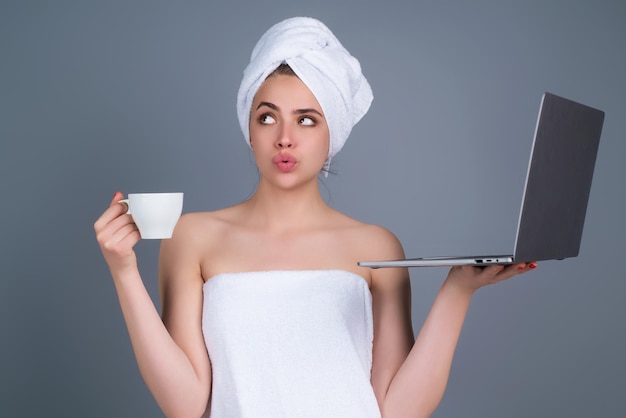 Mujer de negocios independiente de la mañana trabajando en una computadora portátil con una toalla en la cabeza con café trabajando en una computadora portátil