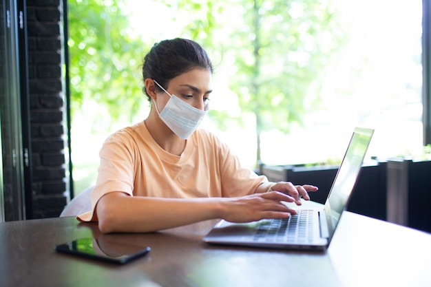 Mujer de negocios india trabajando en su computadora portátil al aire libre con teléfono móvil y mascarilla