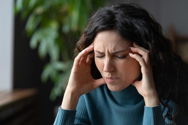 Una mujer de negocios infeliz sufre de un fuerte dolor de cabeza que toca las sienes exhaustas por el estrés en el lugar de trabajo