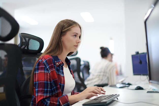 mujer de negocios informal que trabaja en una computadora de escritorio en el moderno interior de la oficina de inicio de planta abierta