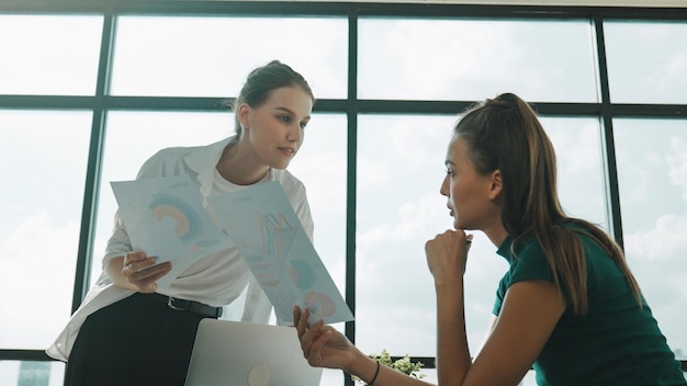 Mujer de negocios inteligente y cooperativa discutiendo sobre la estrategia de negocio Gerente y líder felices compartiendo lluvia de ideas planificando hablando sobre el plan de marketing en una oficina moderna con vista a la ciudad Tracery.