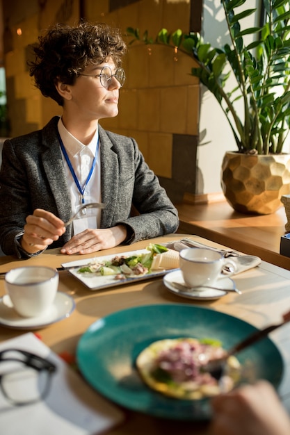 Mujer de negocios inteligente pensativa comiendo ensalada en café