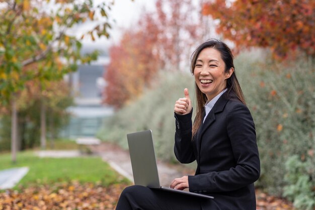 Mujer de negocios japonesa feliz sonriendo y gesticulando con el pulgar hacia arriba