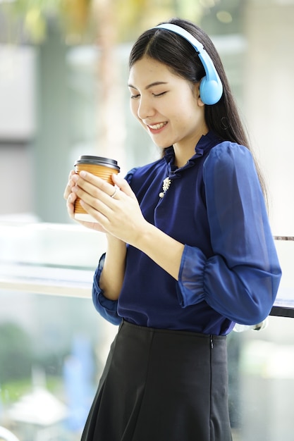 Mujer de negocios joven con auriculares inalámbricos Bluetooth y sosteniendo una taza de café relajarse tim