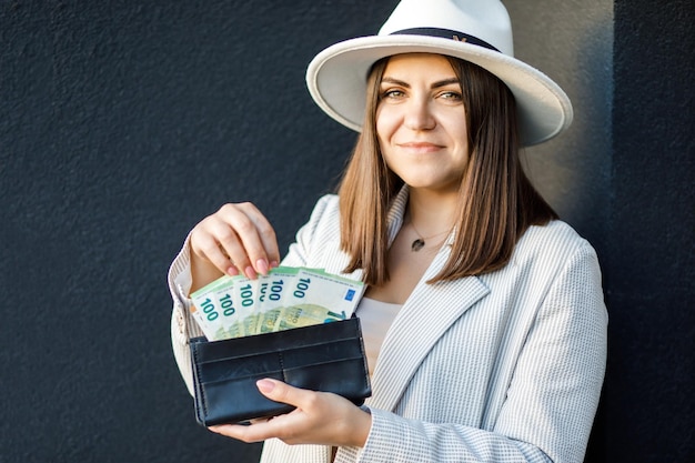 Mujer de negocios joven con billetera negra con billetes en euros cerca de manos femeninas con efectivo El concepto de pagos en efectivo ahorros y salarios