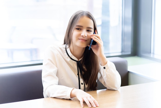 Mujer de negocios joven en un café con un teléfono inteligente hablando sonriendo