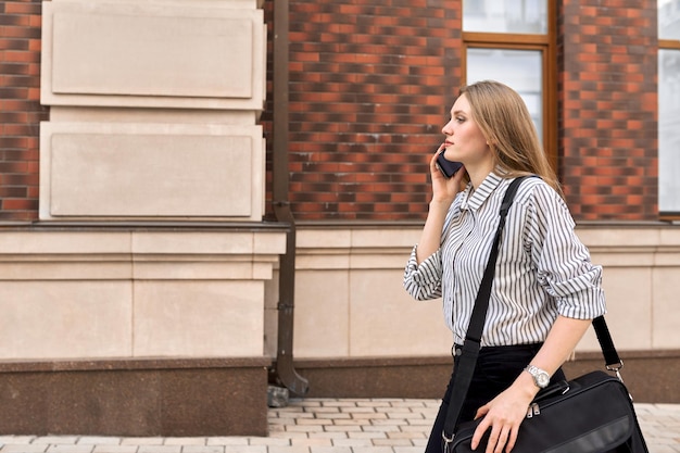 Mujer de negocios joven caminando con el teléfono celular a lo largo de la vista de perfil de la calle de la ciudad espacio de copia de fondo del edificio de ladrillo