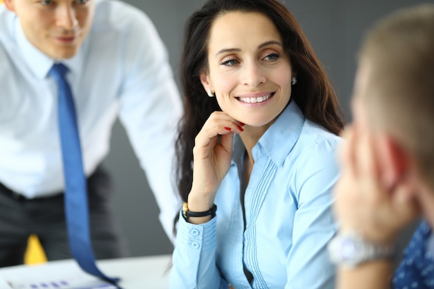 Mujer de negocios joven en camisa azul se comunica con dos hombres en retrato de oficina