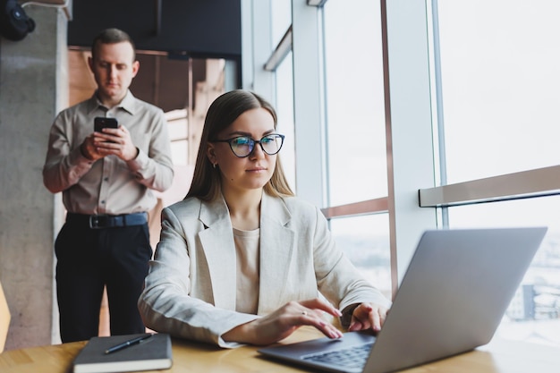 Mujer de negocios joven detrás de una computadora portátil con gafas sentada en una mesa con una reunión de negocios corporativa con colegas en una oficina moderna Concepto de carrera empresarial Enfoque selectivo de espacio libre