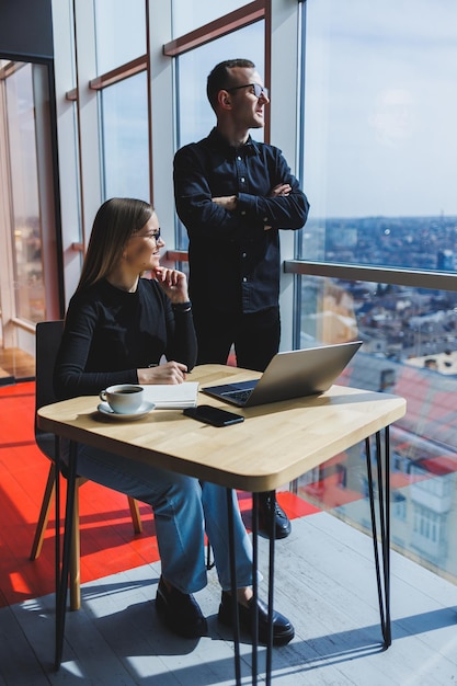 Mujer de negocios joven detrás de una computadora portátil con gafas sentada en una mesa con una reunión de negocios corporativa con colegas en una oficina moderna Concepto de carrera empresarial Enfoque selectivo de espacio libre
