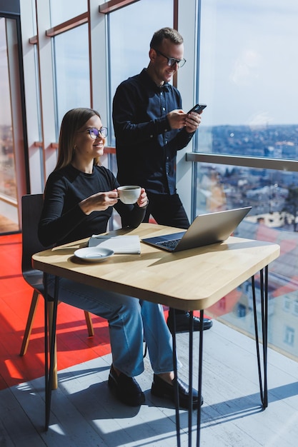 Mujer de negocios joven detrás de una computadora portátil con gafas sentada en una mesa con una reunión de negocios corporativa con colegas en una oficina moderna Concepto de carrera empresarial Enfoque selectivo de espacio libre