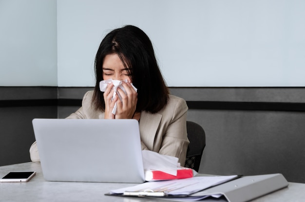 Mujer de negocios joven estornudando mientras trabajaba en la sala de reuniones. Concepto de inflexión estacional y de trabajo.
