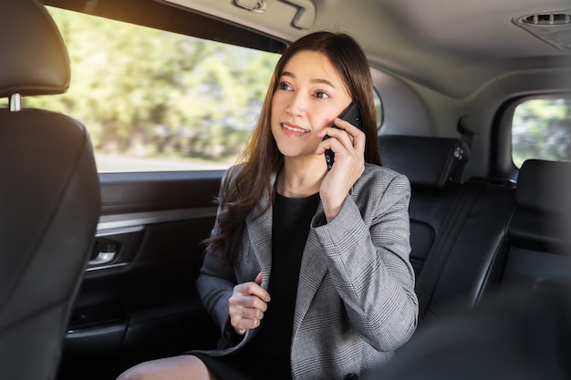 Mujer de negocios joven hablando por teléfono móvil mientras está sentado en el asiento trasero del coche