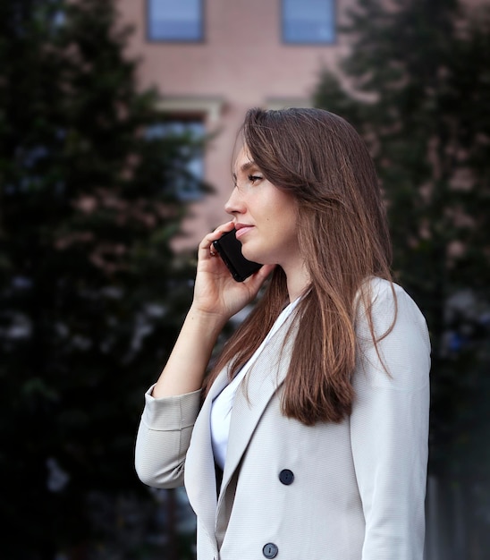 Mujer de negocios joven hablando por teléfono en el primer plano de la ciudad