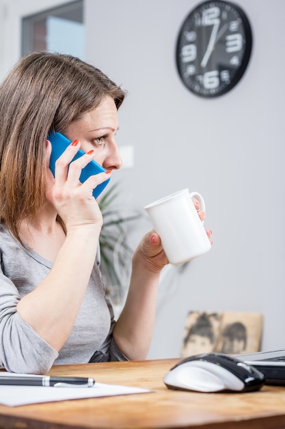 mujer de negocios joven hablando por teléfono y sosteniendo una taza de café