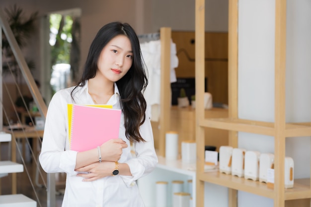 Mujer de negocios joven inteligente vistiendo camisa blanca y jean azul sosteniendo libro rosa de pie delante de la escalera en conceptual de negocio exitoso