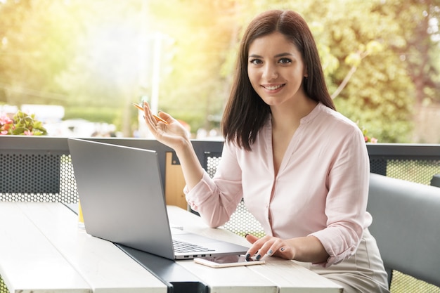 Mujer de negocios joven mirando en el teléfono y sonriendo mientras trabajaba en la computadora.