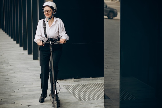 Mujer de negocios joven montando scooter eléctrico por centro de oficina