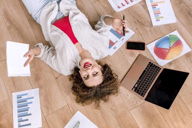 Mujer de negocios joven pensativa sentada en el piso en casa usando una computadora portátil desarrollando un nuevo proyecto