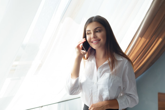 Mujer de negocios joven que habla con el teléfono en el hotel.