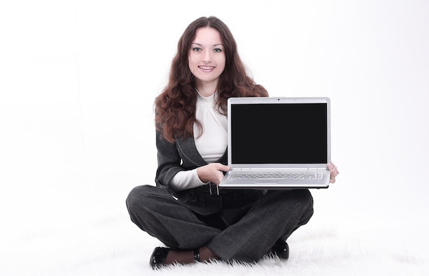 Mujer de negocios joven que muestra una computadora portátil sentada en el suelo