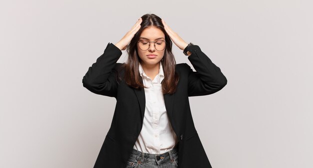 Mujer de negocios joven que parece concentrada, pensativa e inspirada, intercambiando ideas e imaginando con las manos en la frente