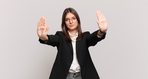 Mujer de negocios joven que parece seria, infeliz, enojada y disgustada prohibiendo la entrada o diciendo que pare con ambas palmas abiertas