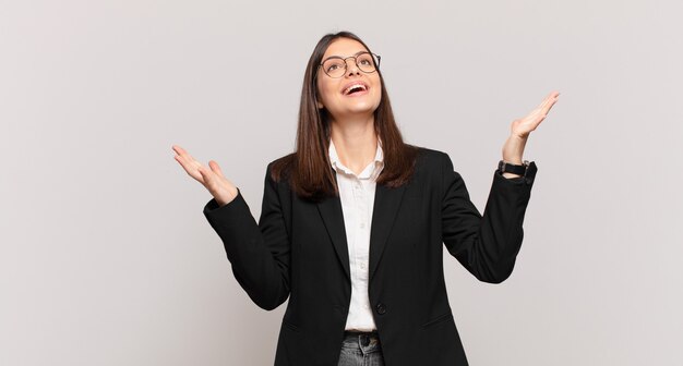 Mujer de negocios joven que se siente feliz, asombrada, afortunada y sorprendida, celebrando la victoria con ambas manos en el aire