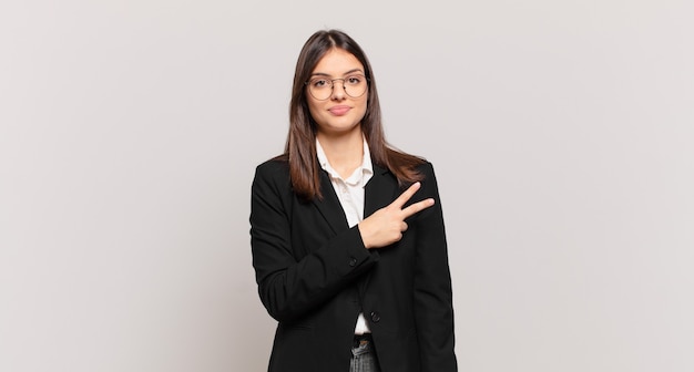 Mujer de negocios joven que se siente feliz, positiva y exitosa, con la mano haciendo forma de v sobre el pecho, mostrando la victoria o la paz