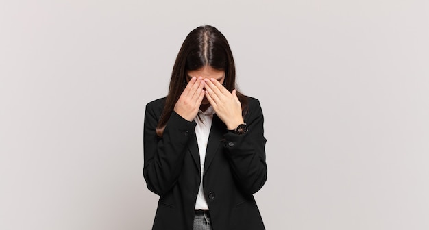 Mujer de negocios joven que se siente triste, frustrada, nerviosa y deprimida, cubriendo la cara con ambas manos, llorando