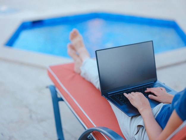 Mujer de negocios joven que trabaja en la computadora junto a la piscina del hotel