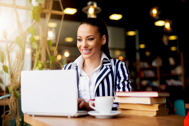 Mujer de negocios joven que trabaja en la computadora portátil en la cafetería.