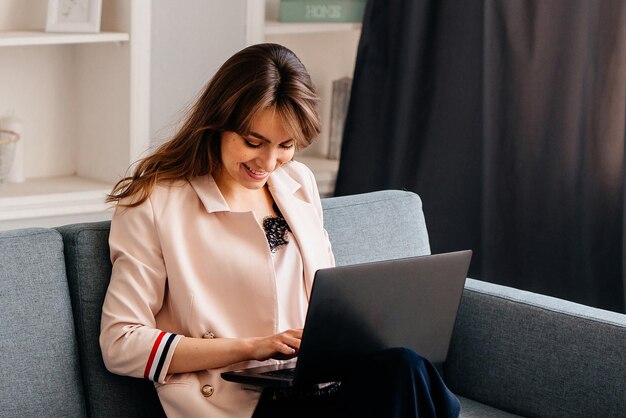 Mujer de negocios joven que usa una computadora portátil sentada en el sofá trabajando desde casa