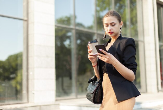 Mujer de negocios joven que usa un teléfono inteligente y toma café mientras viaja al aire libre