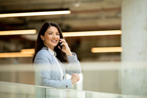 Mujer de negocios joven que usa el teléfono móvil en el pasillo de la oficina