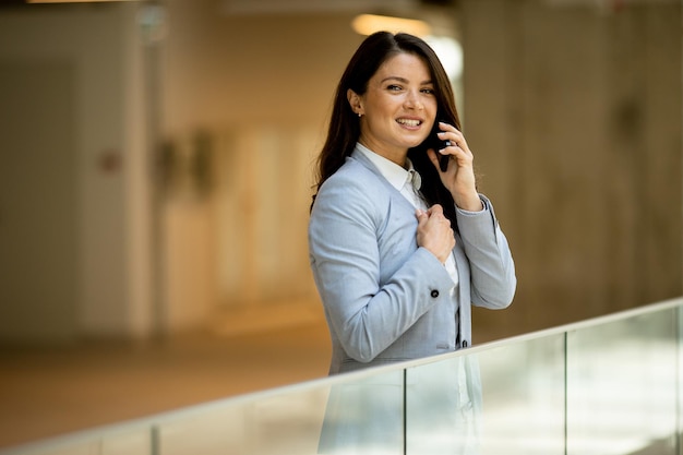 Mujer de negocios joven que usa el teléfono móvil en el pasillo de la oficina