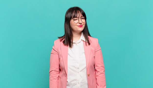 Mujer de negocios joven que se ve feliz y amigable, sonriendo y guiñando un ojo con una actitud positiva