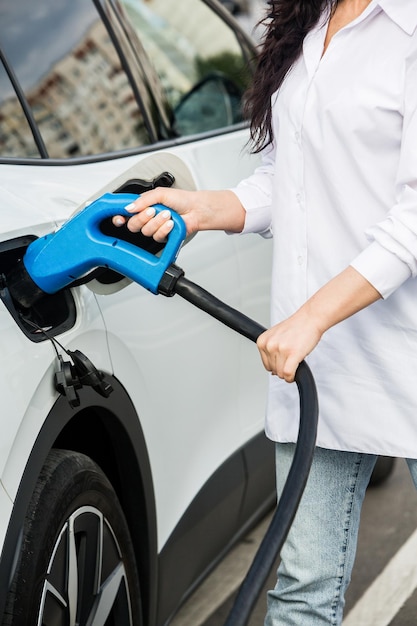 Mujer de negocios joven repostando su coche eléctrico en una estación de carga EV