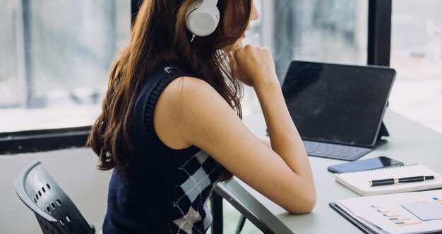 Mujer de negocios joven sentada en la oficina en la mesa y usando un teléfono inteligente En el escritorio hay una computadora portátil y una tableta en gráficos y gráficos de pantalla Mujer analizando datos Estudiante aprendiendo en línea