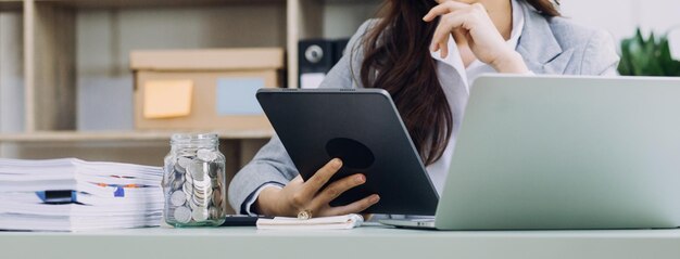 Mujer de negocios joven sentada en la oficina en la mesa y usando un teléfono inteligente En el escritorio hay una computadora portátil y una tableta en gráficos y gráficos de pantalla Mujer analizando datos Estudiante aprendiendo en línea