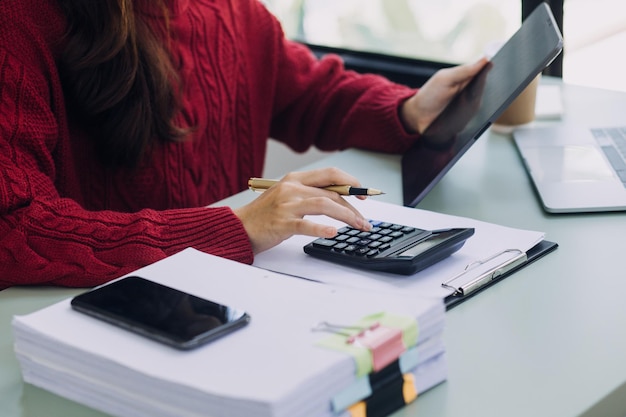 Mujer de negocios joven sentada en la oficina en la mesa y usando un teléfono inteligente En el escritorio hay una computadora portátil y una tableta en gráficos y gráficos de pantalla Mujer analizando datos Estudiante aprendiendo en línea