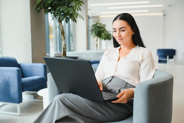 Mujer de negocios joven sentada en el sofá y trabajando con una computadora portátil en la sala de espera del centro de negocios