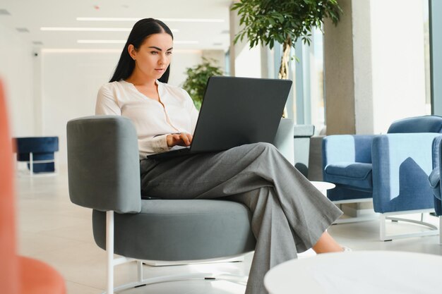 Mujer de negocios joven sentada en el sofá y trabajando con una computadora portátil en la sala de espera del centro de negocios