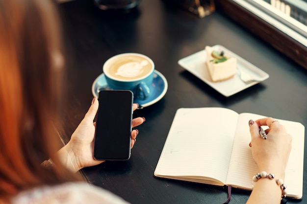 Mujer de negocios joven sentado a la mesa en una cafetería y tomar notas