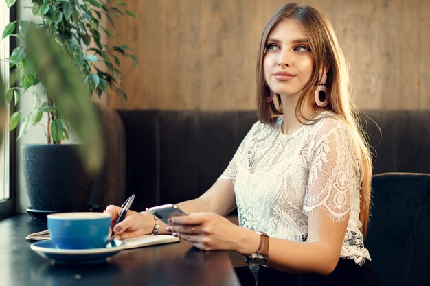 Mujer de negocios joven sentado a la mesa en una cafetería y tomar notas