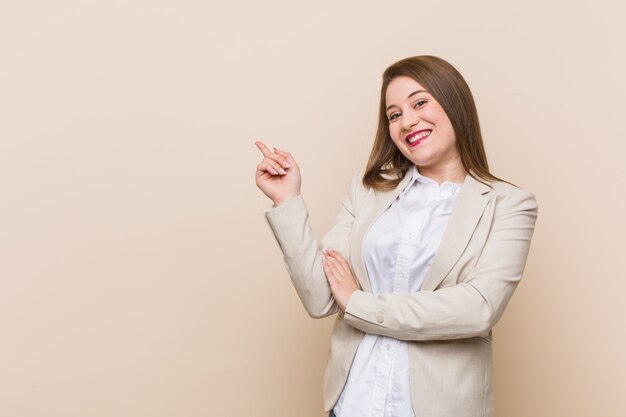 Mujer de negocios joven sonriendo alegremente señalando con el dedo lejos.